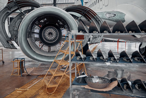 Plane being serviced in hangar with parts from distributors that use aircraft spare parts inventory management software.