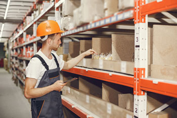 Warehouse worker in warehouse going through bins for parts on shelves learns how to organize parts inventory using a bin system.