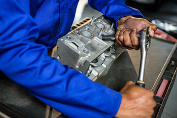 Person repairing engine part in a repair shop, a critical player in the auto parts supply chain