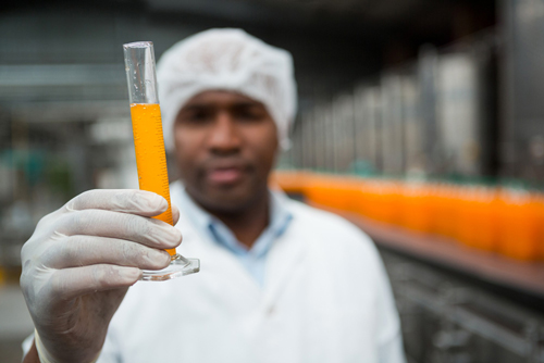 Beverage manufacturing software by Acctivate Worker in juice factory showing a test tube of juice produced with beverage manufacturing software from Acctivate