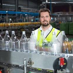 Beverage manufacturing software tracks juice in production line Worker at juice bottling factory stands behind empty bottles in production line being tracked with beverage manufacturing software