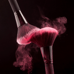 Makeup brushes with pink powder swirling together represent cosmetic products being tracked throughout manufacturing procedures with cosmetics manufacturing software