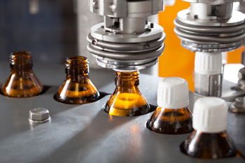 Production machine caps bottles with medicine made with pharmaceutical manufacturing inventory software