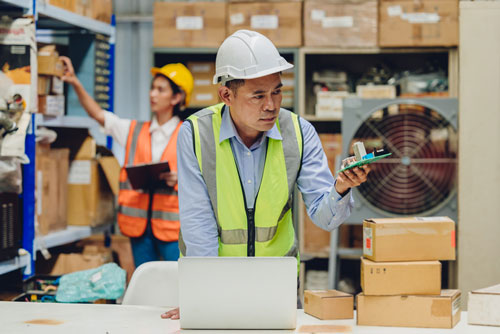 Worker in a warehouse checks an electrical product from a supplier and uses an ERP system for electrical distributors