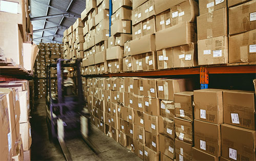 A forklift moving through a warehouse aisle of shelves packed with inventory