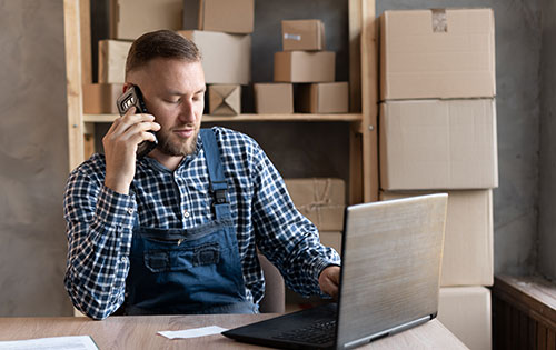 Person on the phone and laptop in a warehouse preforming a price check for a customer