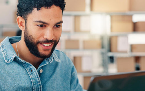 Person smiling looking at a computer screen in a warehouse as they look for inventory software for small businesses